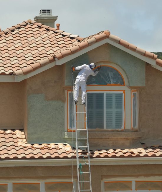 Worker leaning dangerously off the ladder to paint the stucco on